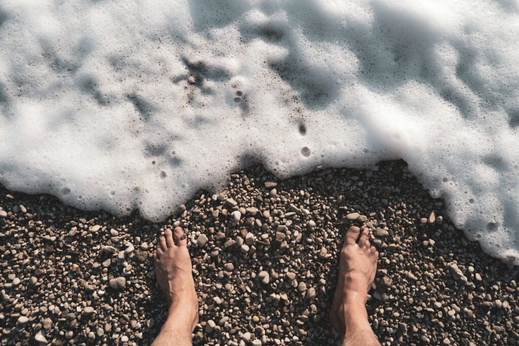 Los pies de una persona sobre la arena a la orilla del mar 